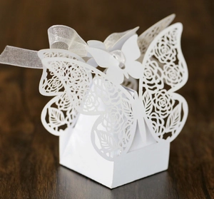 Detail of laser-cut white butterfly candy box with rose patterns on wooden surface