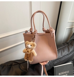 Pink lychee grain leather bucket bag featuring woven knot handles and cute teddy bear charm