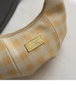 Close-up of yellow checkered crescent bag showing leather texture and fashion brand label