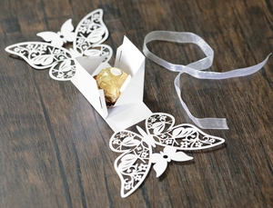 Macro detail of white laser-cut butterfly wedding favor box with chocolate inside
