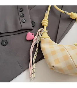 Detail of yellow checkerboard crescent bag with pink heart and colorful woven charms