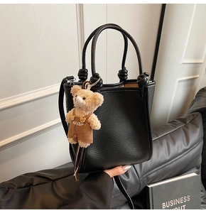 Detail of black lychee grain bucket bag with a cute plush bear charm on a leather sofa
