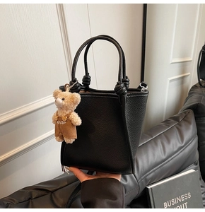 Detail of black lychee-textured winged bucket bag featuring a cute teddy bear charm