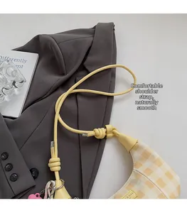 Detail of checkered shoulder bag featuring a unique knotted strap and heart charm