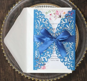 Dettaglio dell'invito blu glitterato con nastro blu scuro e inserto con motivi floreali