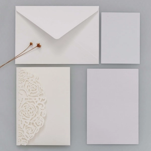 Détails de motifs de roses découpés au laser sur invitations de mariage blanc crème