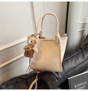 Close-up of beige lychee texture bucket bag with a cute brown bear charm accessory