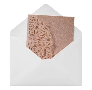 Macro detail of laser-cut rose gold glitter wedding invitation with white envelope