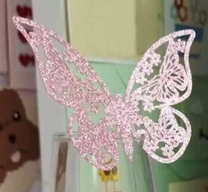 Mariposa 3D rosa con purpurina y diseño calado colgada en el borde de un vaso decorativo