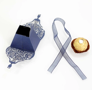 Detail of dark blue laser-cut candy box with floral pattern and ribbon for wedding favors