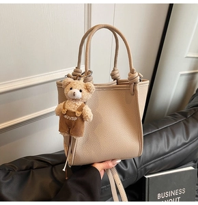 Detail of beige lychee grain leather bucket bag with knot handle and cute bear charm