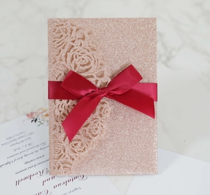 Detail of rose gold glitter laser cut wedding invitation with burgundy silk bow decoration
