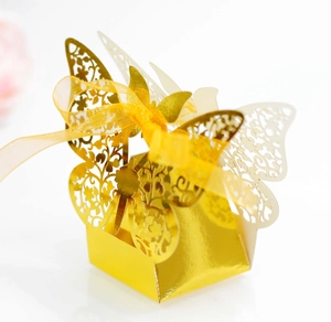 Detail of laser-cut butterfly wedding favor box in metallic gold with organza ribbon