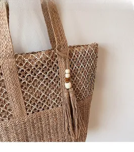 Detail showing woven texture and decorative tassel with wooden beads on the straw tote bag