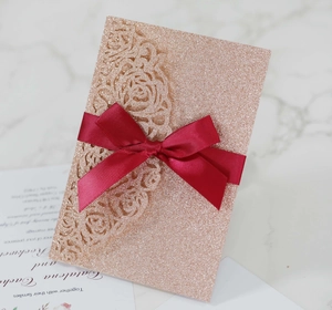 Detail of laser-cut rose gold glitter invitation with burgundy ribbon on marble surface