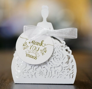 Detail of white laser-cut bridal dress favor box with ribbon and Thank You gold foil tag