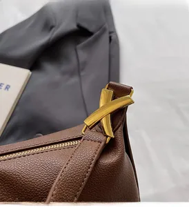 Detail of brown lychee leather shoulder bag featuring a gold X-shaped metal buckle