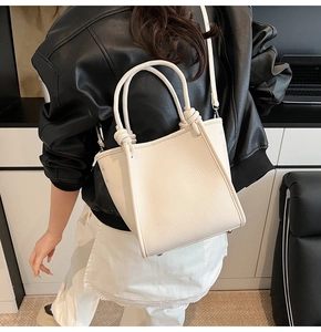 Close-up of cream textured leather bucket bag with twisted handle and silver hardware