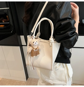 Close-up of white lychee pattern leather bucket bag with cute bear charm and knot handle