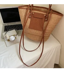 Detail of large straw woven tote bag featuring brown leather trim and sturdy handles