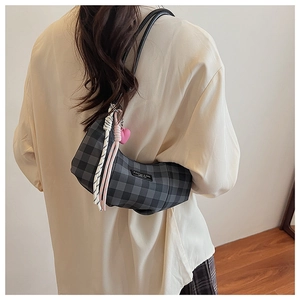Detail of grey checkered crescent bag with pink heart pendant worn on the shoulder