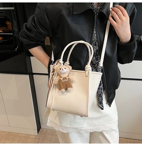 Close-up of beige lychee texture tote bag with brown plush bear charm and crossbody strap