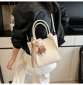 Close-up of cream lychee leather handbag with cute bear charm and tassel detail