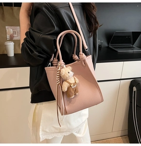 Close-up of pink litchi grain leather bucket bag with a cute plush bear charm accessory