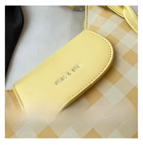 Detail of yellow checkered canvas bag with leather flap and embossed logo stitching