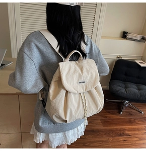 Cream nylon backpack featuring a drawstring closure and minimalist rubber logo patch