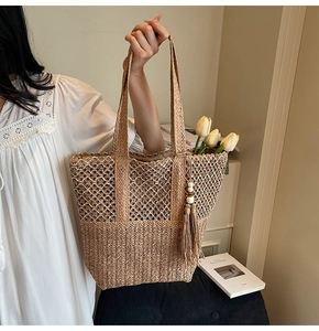 Detail of woven straw tote bag featuring mixed knit textures and a wooden bead tassel