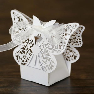 White laser-cut butterfly wedding favor box with ribbon on dark wood surface