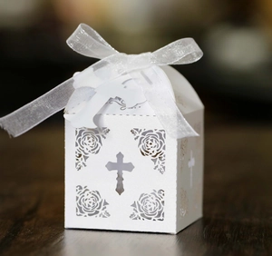 Detail of white laser-cut cross wedding candy box with floral patterns and organza ribbon
