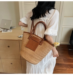 Detail of large straw woven tote bag with brown leather handles worn by a model