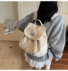 Detail view of cream nylon drawstring backpack with flap design in a lifestyle office setting