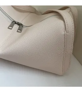 Detailed macro view of off-white lychee leather texture and dual silver zippers on the bag