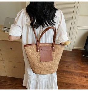 Detail of hand-woven straw tote bag with brown faux leather straps and front pocket