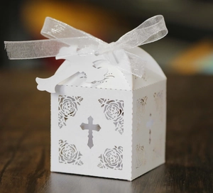 Detail of laser-cut white favor box with rose patterns and cross charm on wood background