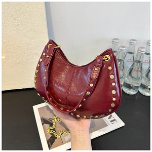 Macro shot of burgundy half-moon bag with golden rivets and metallic chain strap