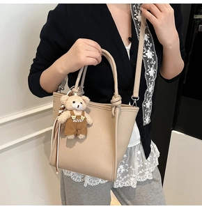 Detail of beige lychee texture leather bucket bag with cute bear charm and shoulder strap