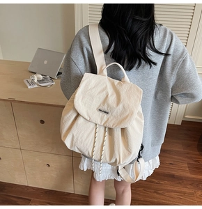 Close-up of cream nylon backpack featuring flap closure and woven bear logo detail