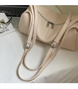 Detail view of cream leather cylinder bag with dual zippers and adjustable strap