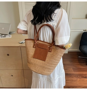 Detail of hand-woven straw tote bag with brown leather pocket and handles in a cozy setting