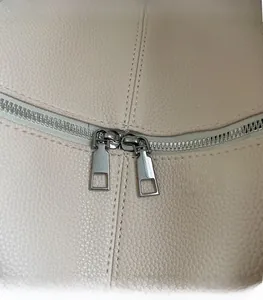 Detail of silver dual metal zippers on creamy beige lychee textured leather handbag