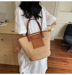 Detail of hand-woven straw tote bag with brown leather pocket on white dress model