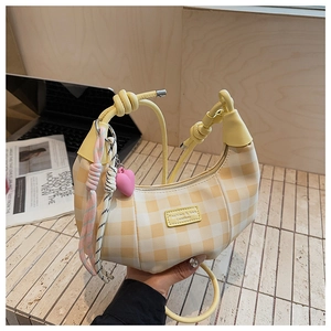 Detail of yellow checkered crescent bag with knotted strap and heart charm on a desk