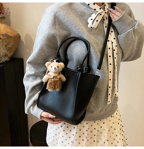 Detail of black litchi grain bucket bag with cute bear charm and long shoulder strap