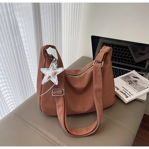 Detail view of brown knitted tote bag with silver star charm on a leather bench