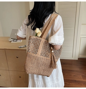 Detail of woven straw tote bag featuring mesh stitching and tassel charm for beach vacations