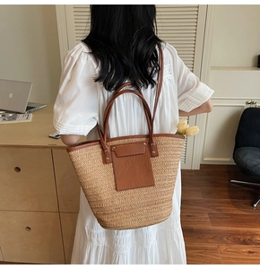 Detail view of woven straw tote bag with brown faux leather straps shown in lifestyle setting